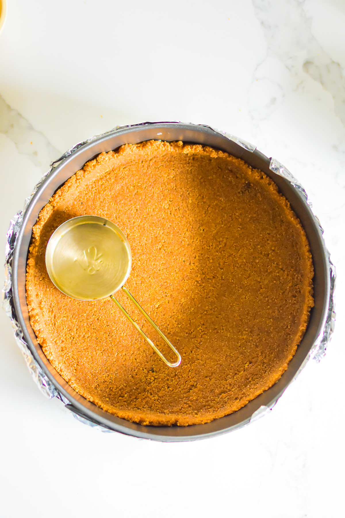 scratch-made graham cracker crust pressed into springform pan with a measuring cup.