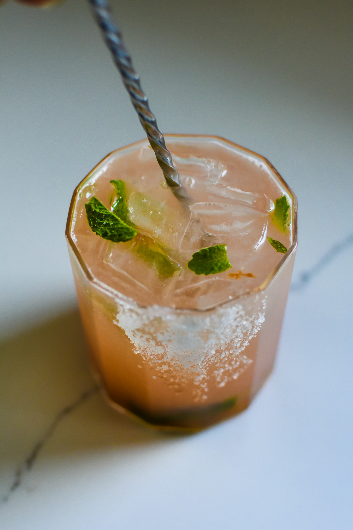 stirring pink grapefruit mocktail with fresh mint, ice, and honey using bar spoon.