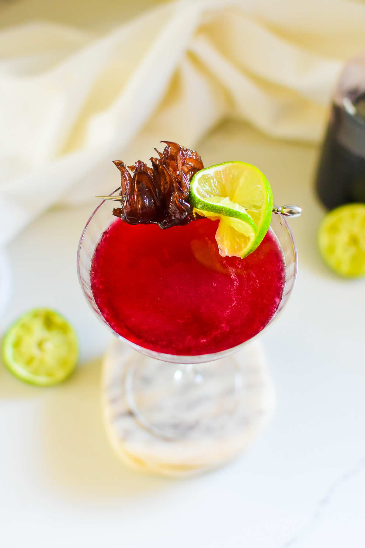 freshly made hibiscus-tini surrounded by halves of lime and bottle of sorrel syrup.