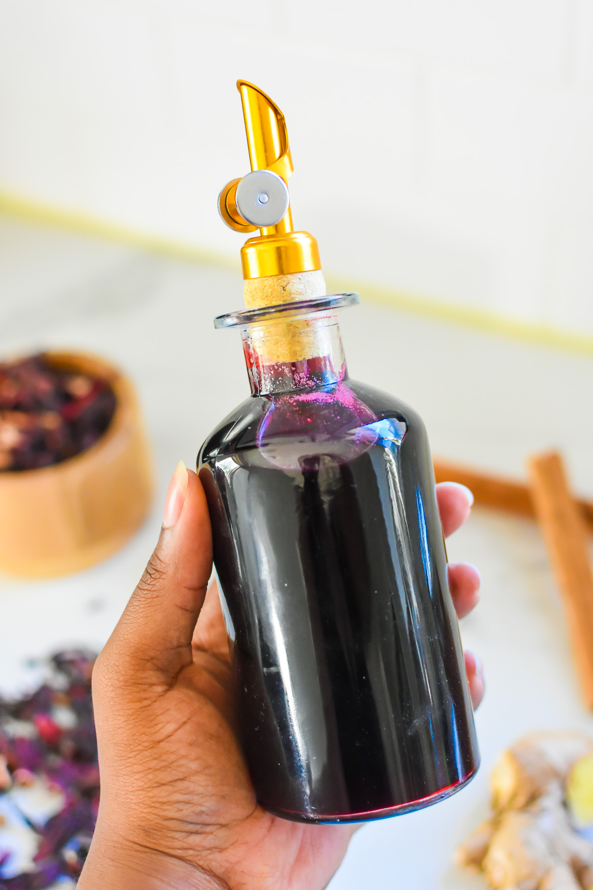 brown hand holding glass bottle of DIY hibiscus ginger syrup.