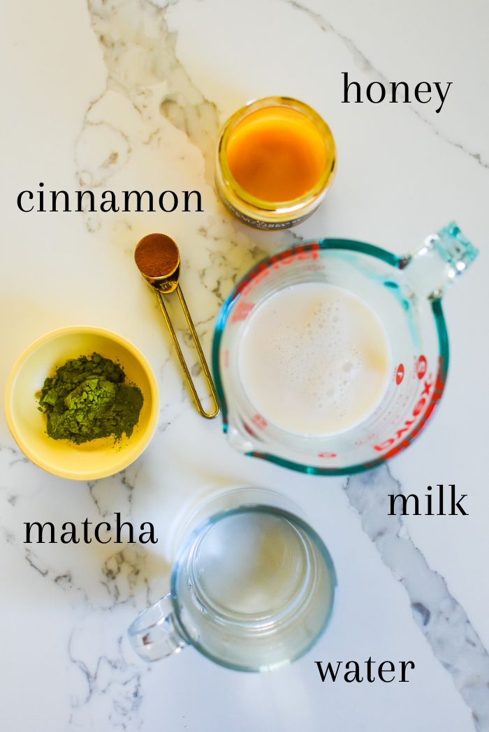 ingredients to make the best DIY cinnamon matcha latte on counter top, including honey, ground cinnamon, plant based milk, organic ceremonial grade matcha powder, and hot water.