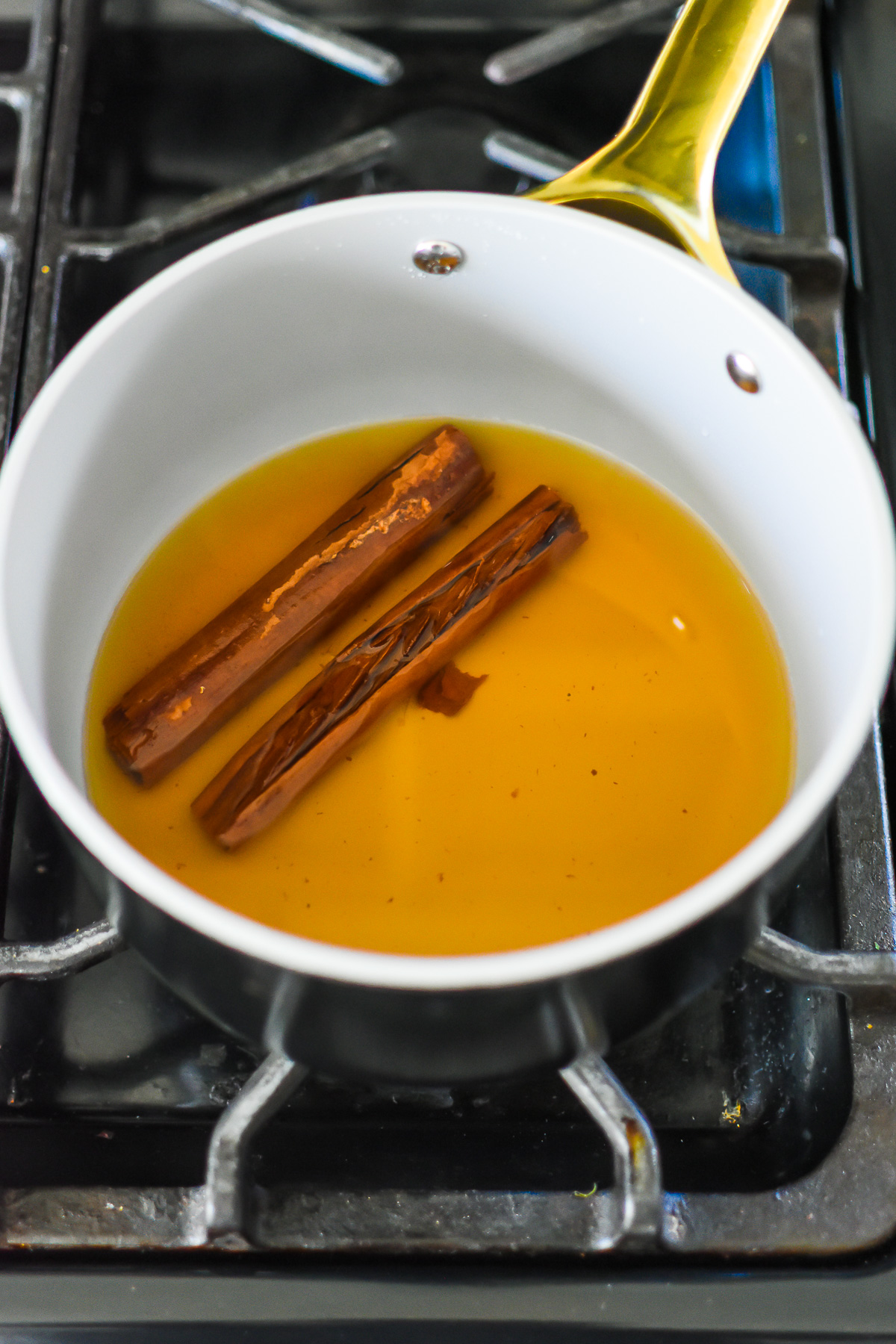 two cinnamon sticks steeping in boiled water on stove top.