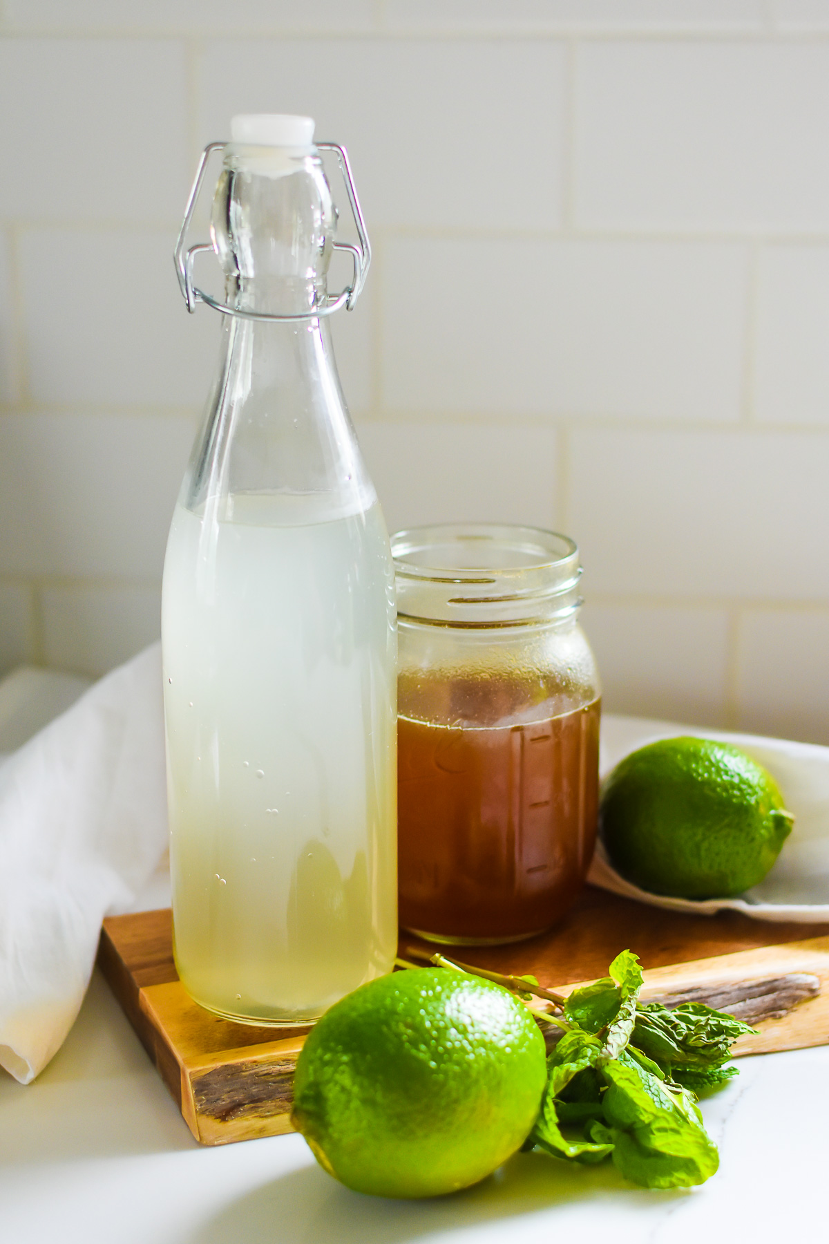 ingredients to make a coconut electrolyte mocktail on counter top, including fresh coconut water, ginger honey syrup, limes, and mint.