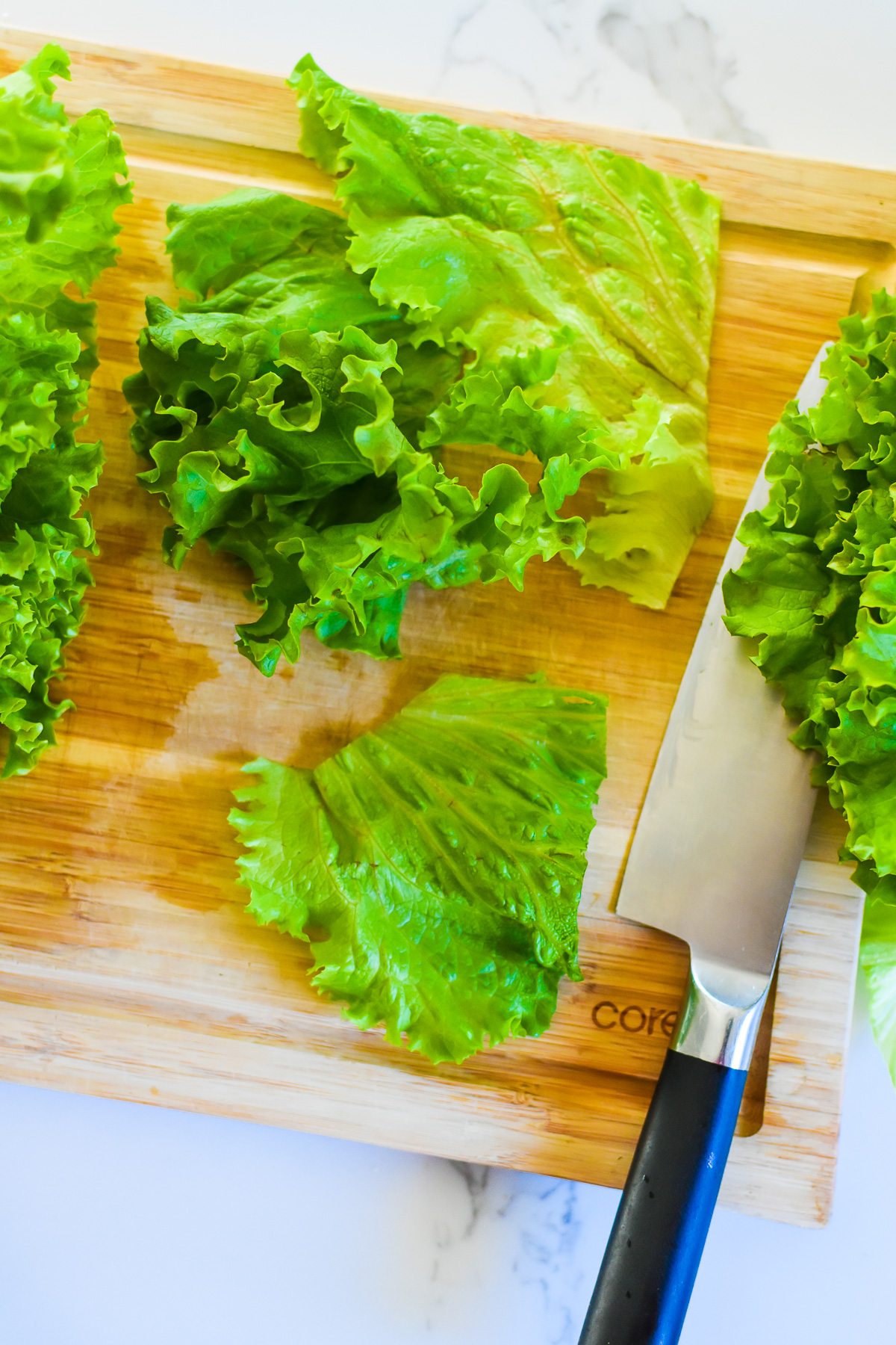 pieces of green leaf lettuce and knife on cutting board.