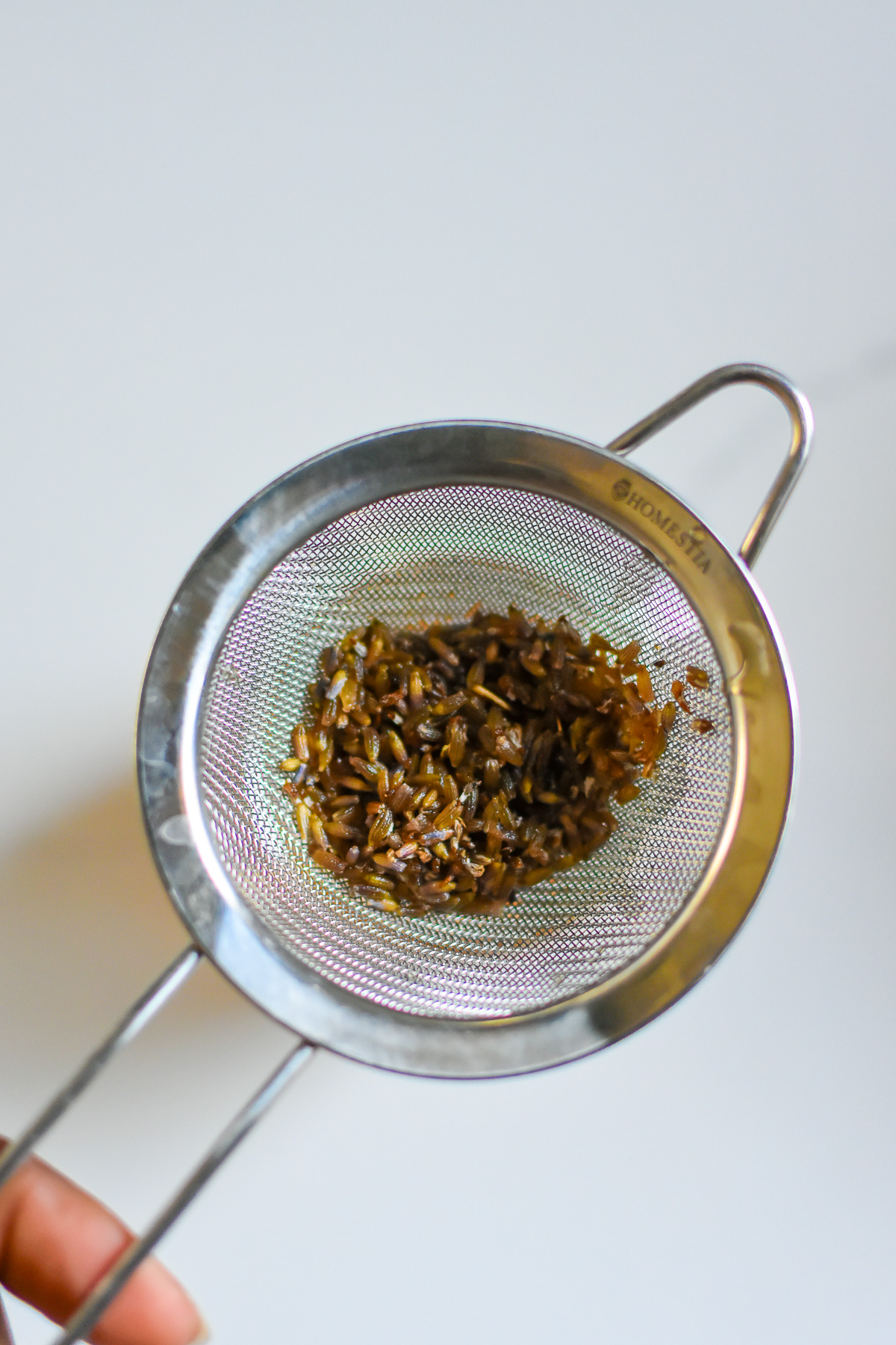honey soaked lavender syrup in silver mesh strainer.