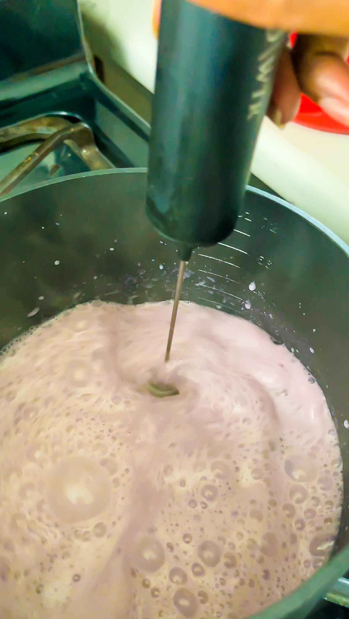 mixing steaming hibiscus latte with coconut milk with frothing wand in saucepan.