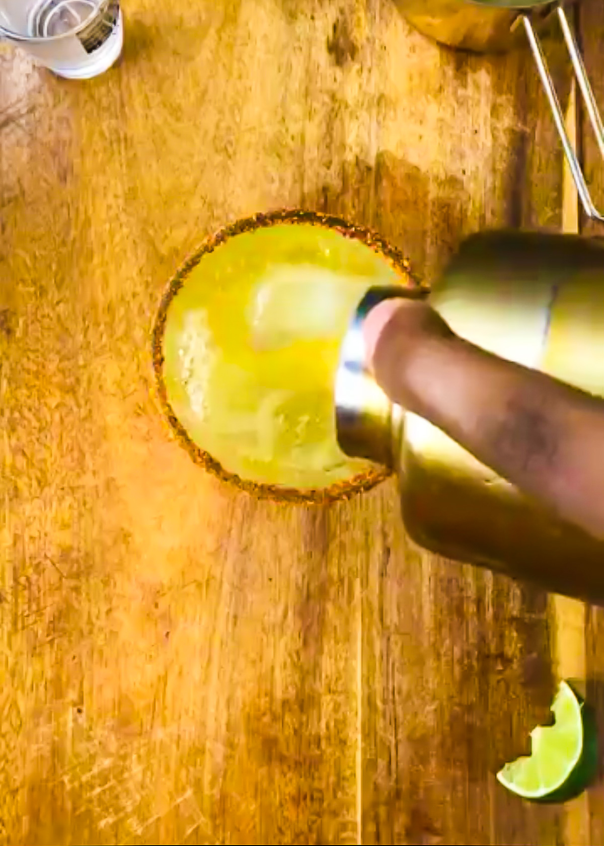 pouring homemade passion fruit juice margarita from gold cocktail shaker into spicy rimmed glass over ice.