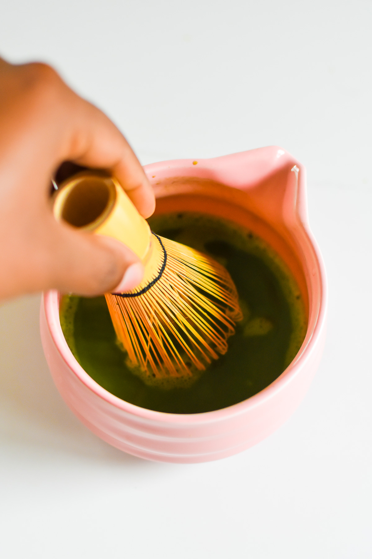 whisking matcha powder and hot water together in pink ceramic bowl.