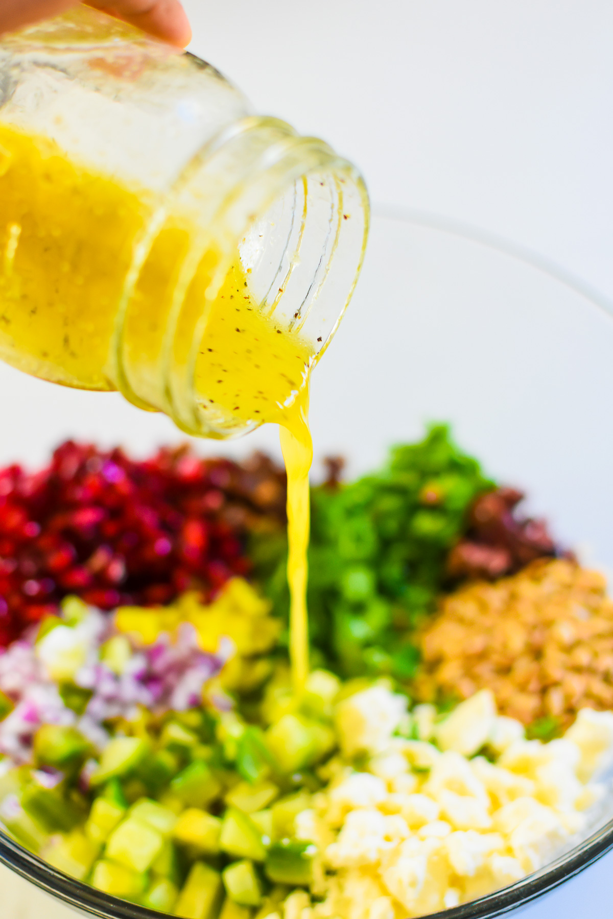 pouring ACV dressing over chopped Mediterranean salad ingredients.