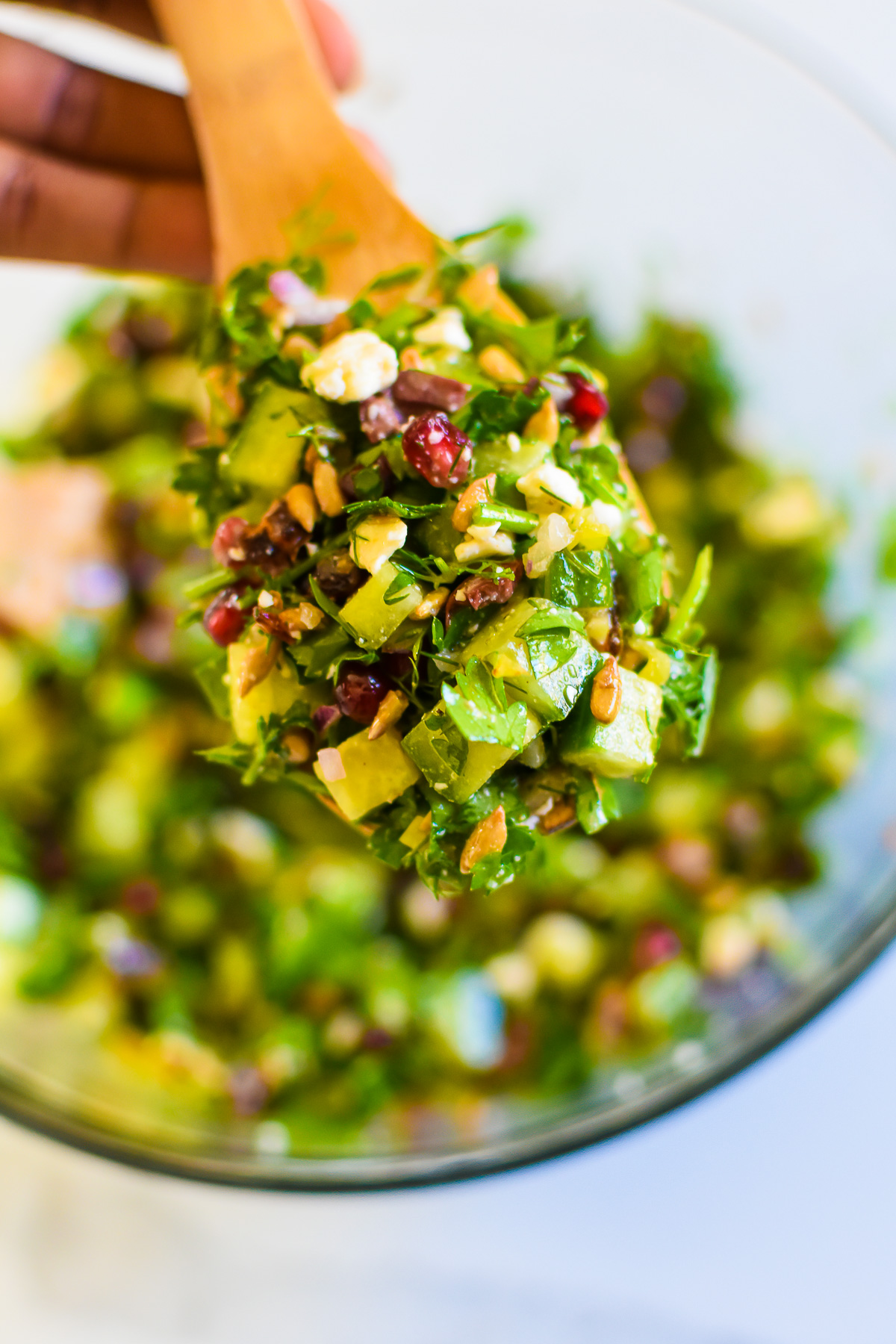 spoonful of chopped cucumbers, herbs, pomegranate, feta cheese, seeds, dates, olives, and peppers dressed in simple vinaigrette.