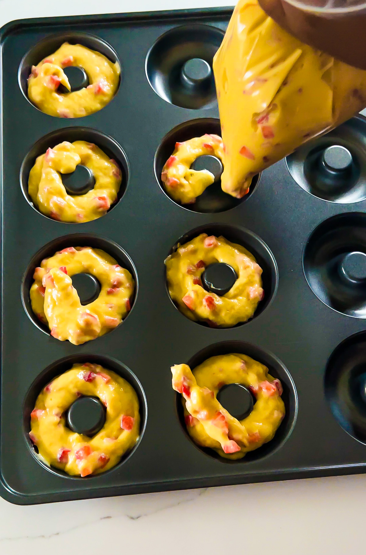 piping Valentine strawberry donut batter into cake donut pan.