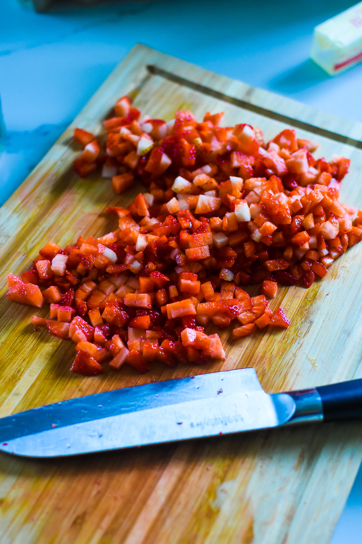 diced fresh strawberries on wooden cutting board with knife.