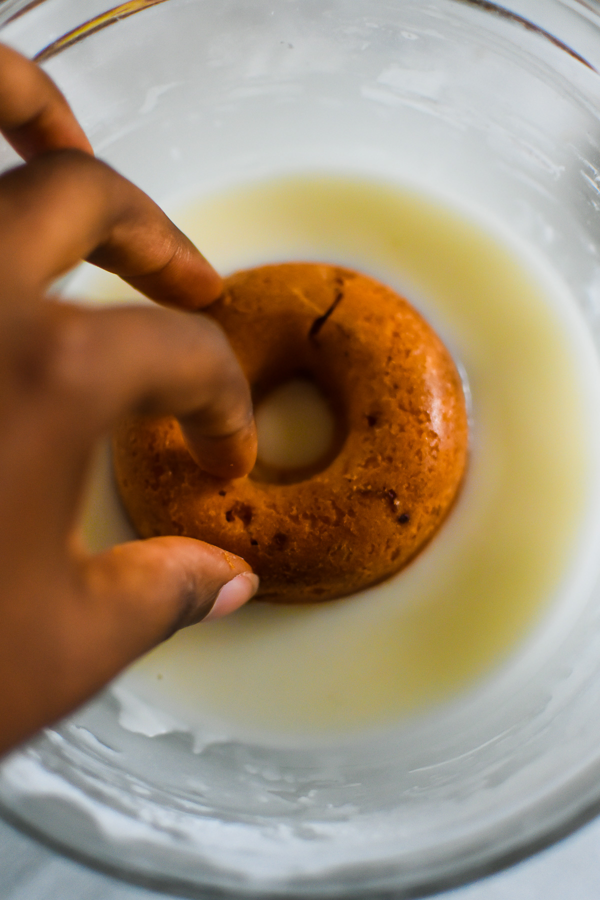 brown hand dipping baked donut in champagne glaze.