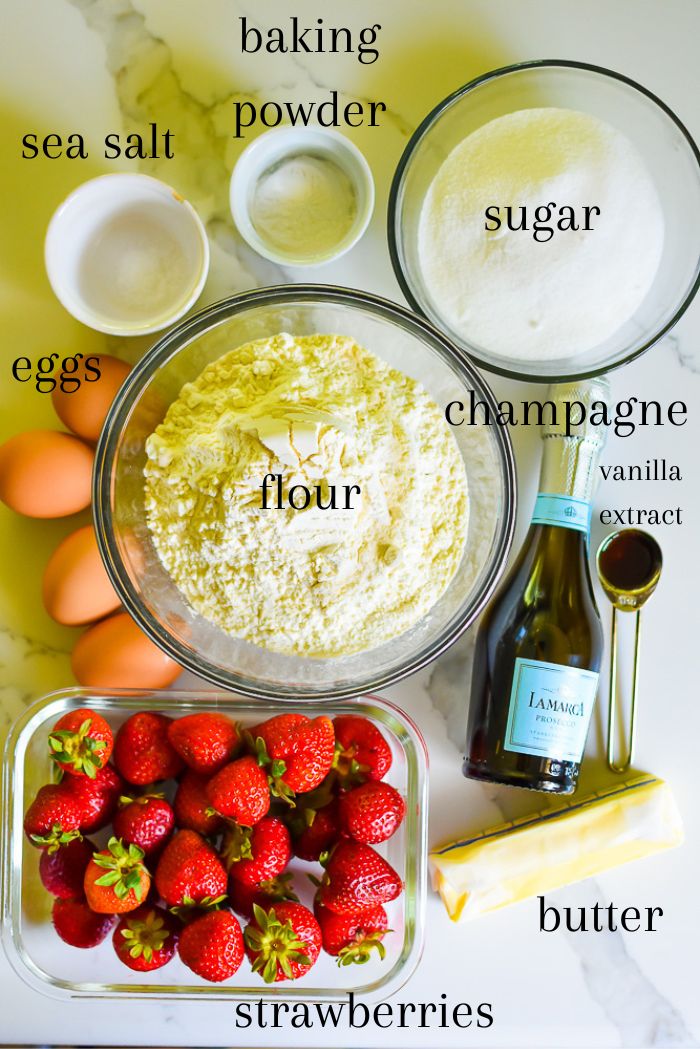 ingredients to make easy Valentine's Day donuts at home on granite counter top, including flour, eggs, strawberries, butter, vanilla, champagne, sugar, baking powder, sea salt, and powdered sugar.