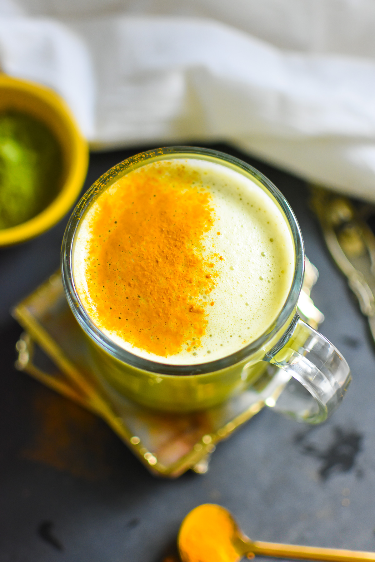 hot turmeric matcha latte in glass mug with ground turmeric sprinkled over top.