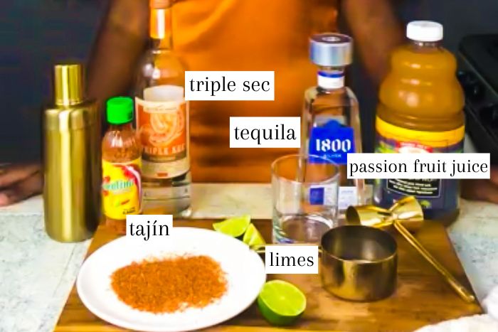 ingredients to make an easy spicy passion fruit margarita at home on counter top, including triple sec, 1800 tequila, passion fruit juice, fresh limes, tajín, and ice.