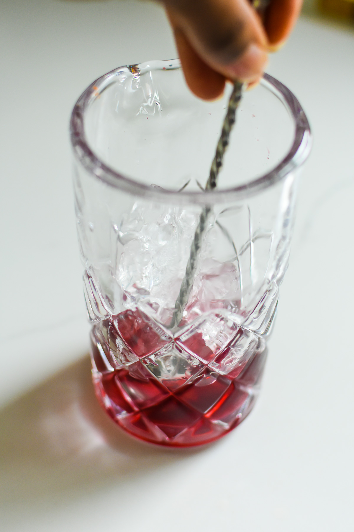 stirring bourbon, ice, hibiscus syrup, and bitters together.