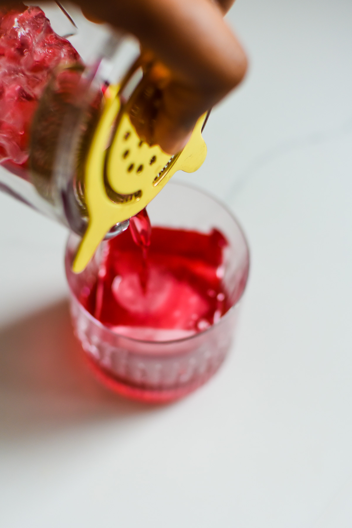 straining old fashioned with hibiscus simple syrup into rocks glass over big cube of ice.
