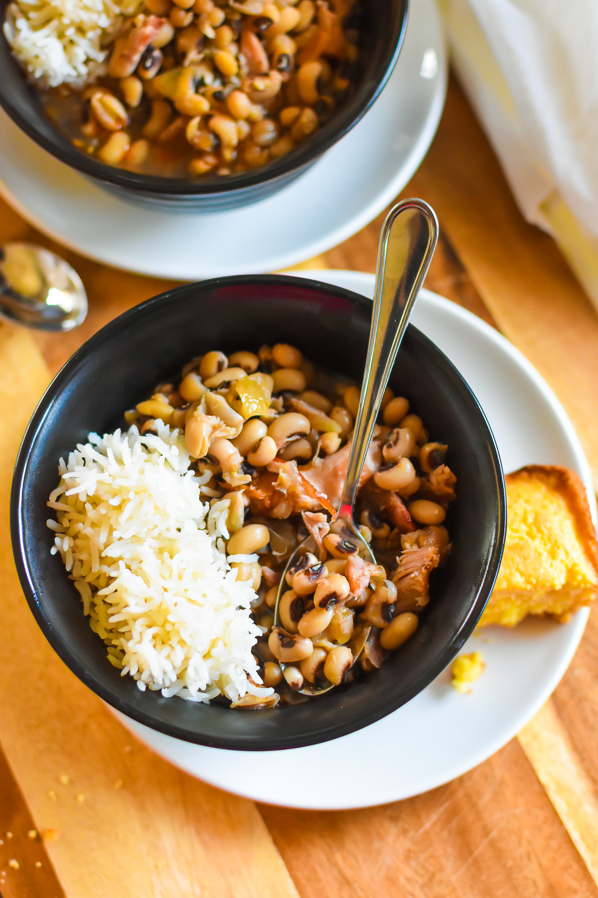 Authentic Soul Food black eyed peas served in black stone bowls with scoops of fluffy white rice and squares of golden cornbread.