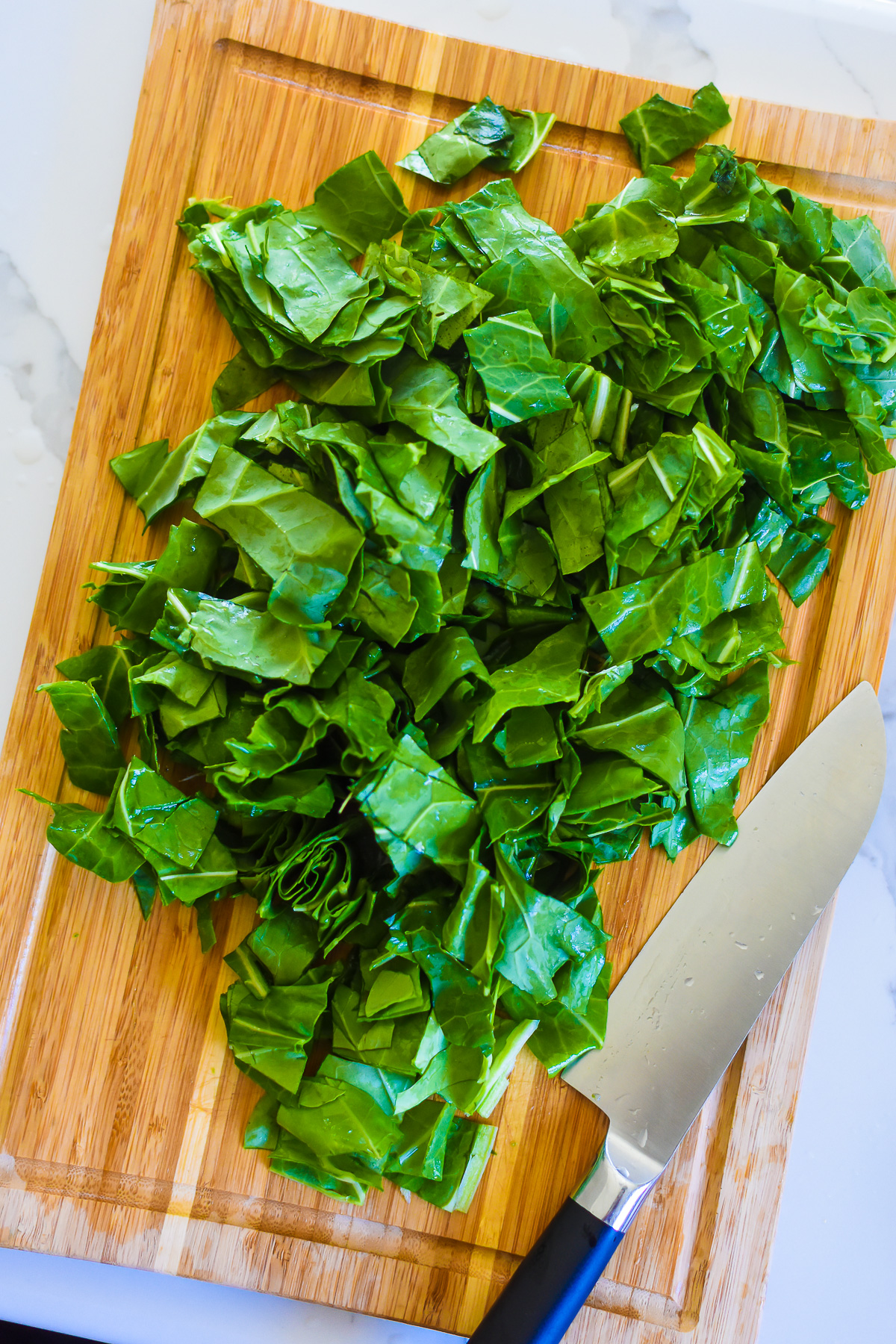 washed, stemmed, and chopped collard greens on a wooden cutting board next to a sharp knife.