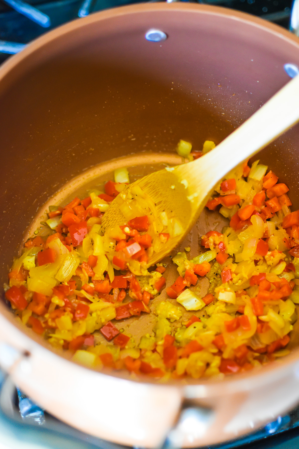 diced onion, red bell pepper, and crushed garlic sautéing in olive oil and spices in a deep copper pot.