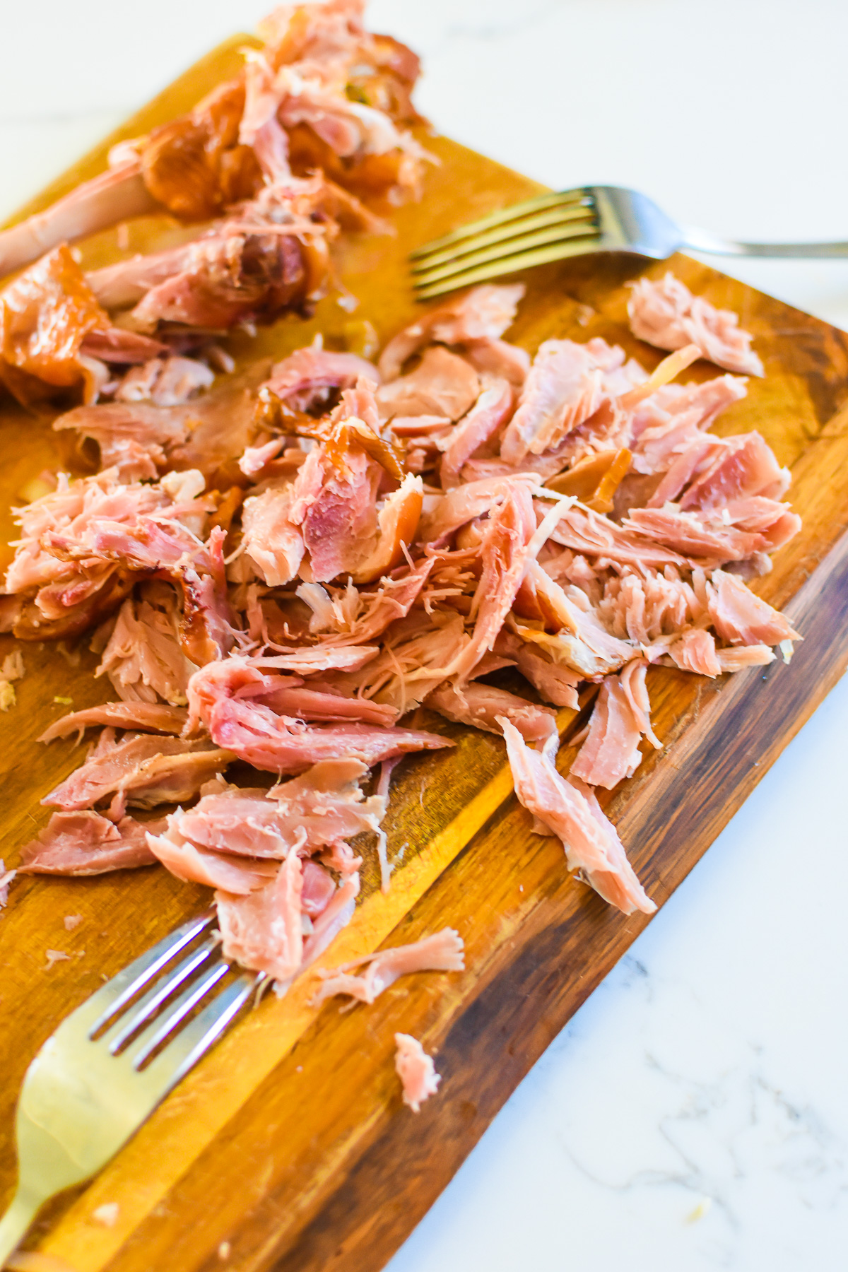 smoked turkey drum meat shredded from the bone on a wooden cutting board next to two forks.