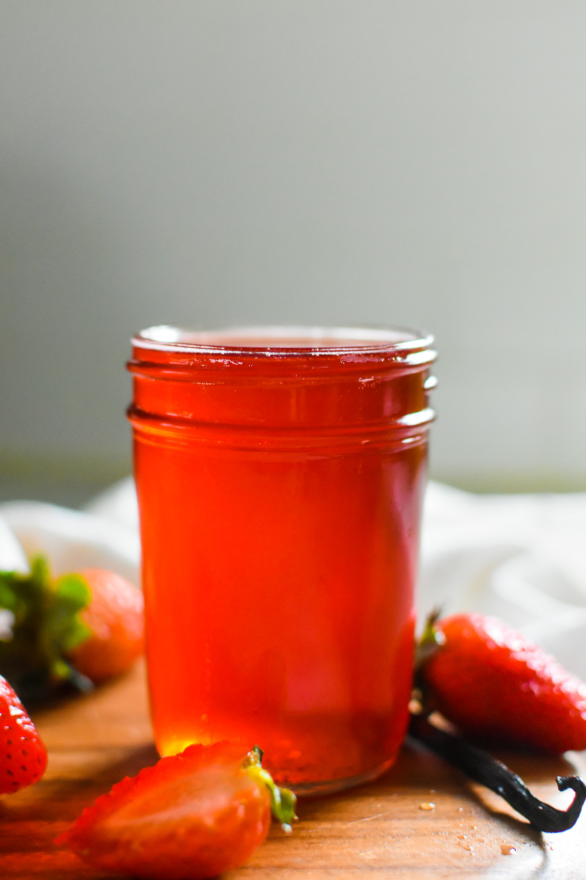 DIY simple strawberry syrup in jar surrounded by fresh strawberries and a vanilla bean.