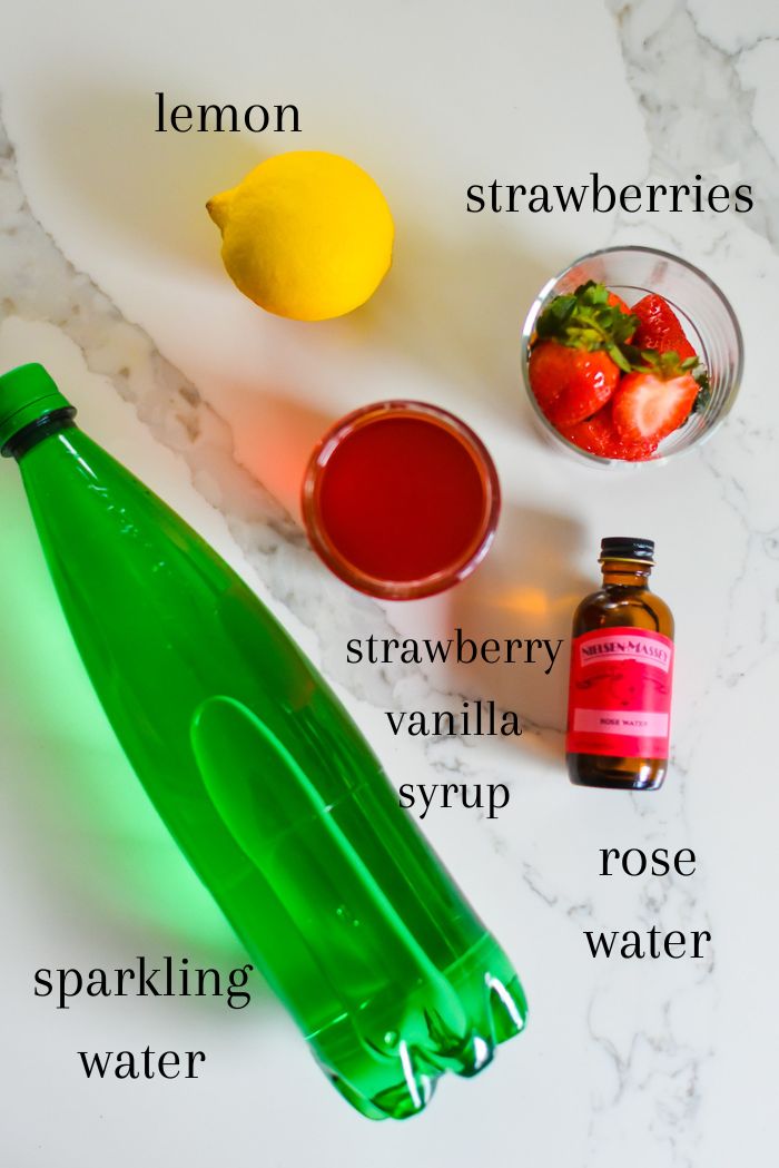 ingredients to make an easy Valentine's mocktail at home on granite counter top, including sparkling water, strawberry vanilla syrup, rose water, strawberries, and lemon.