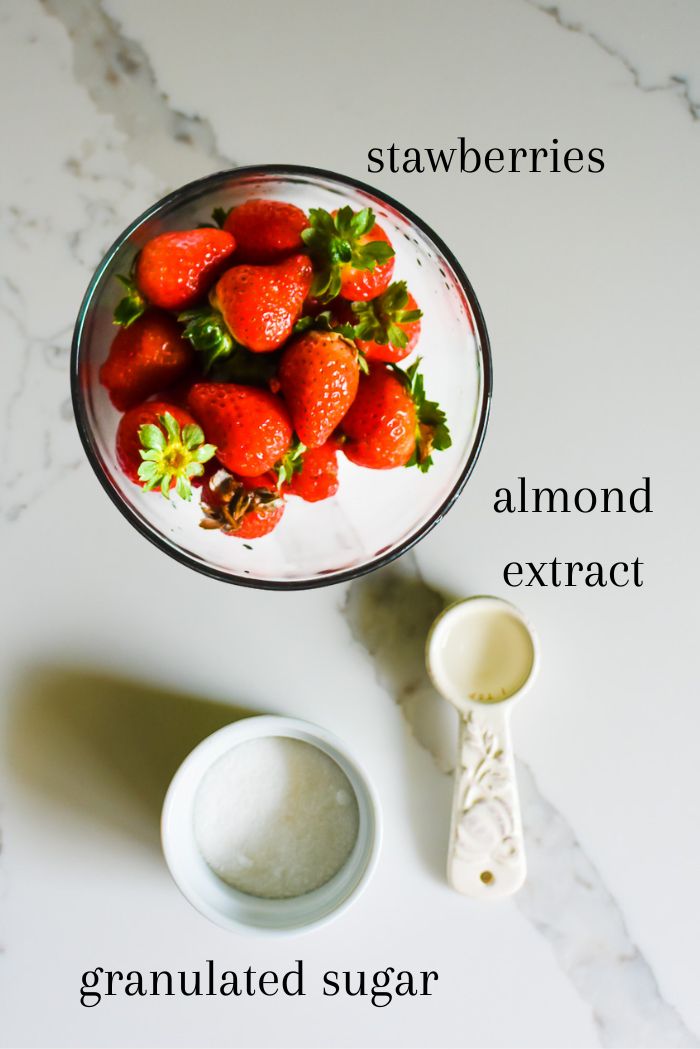ingredients for macerated strawberries on granite counter top: fresh whole strawberries, almond extract, and granulated sugar.