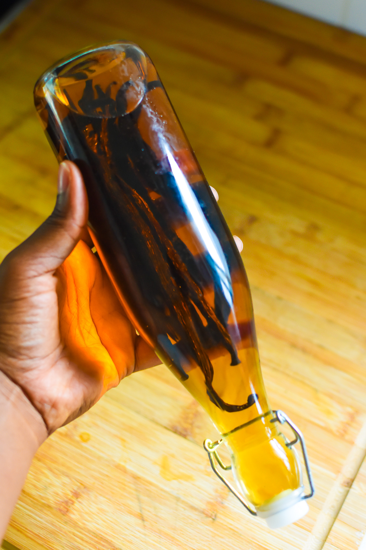 brown hand shaking glass bottle filled with vanilla extract to aid in infusion.