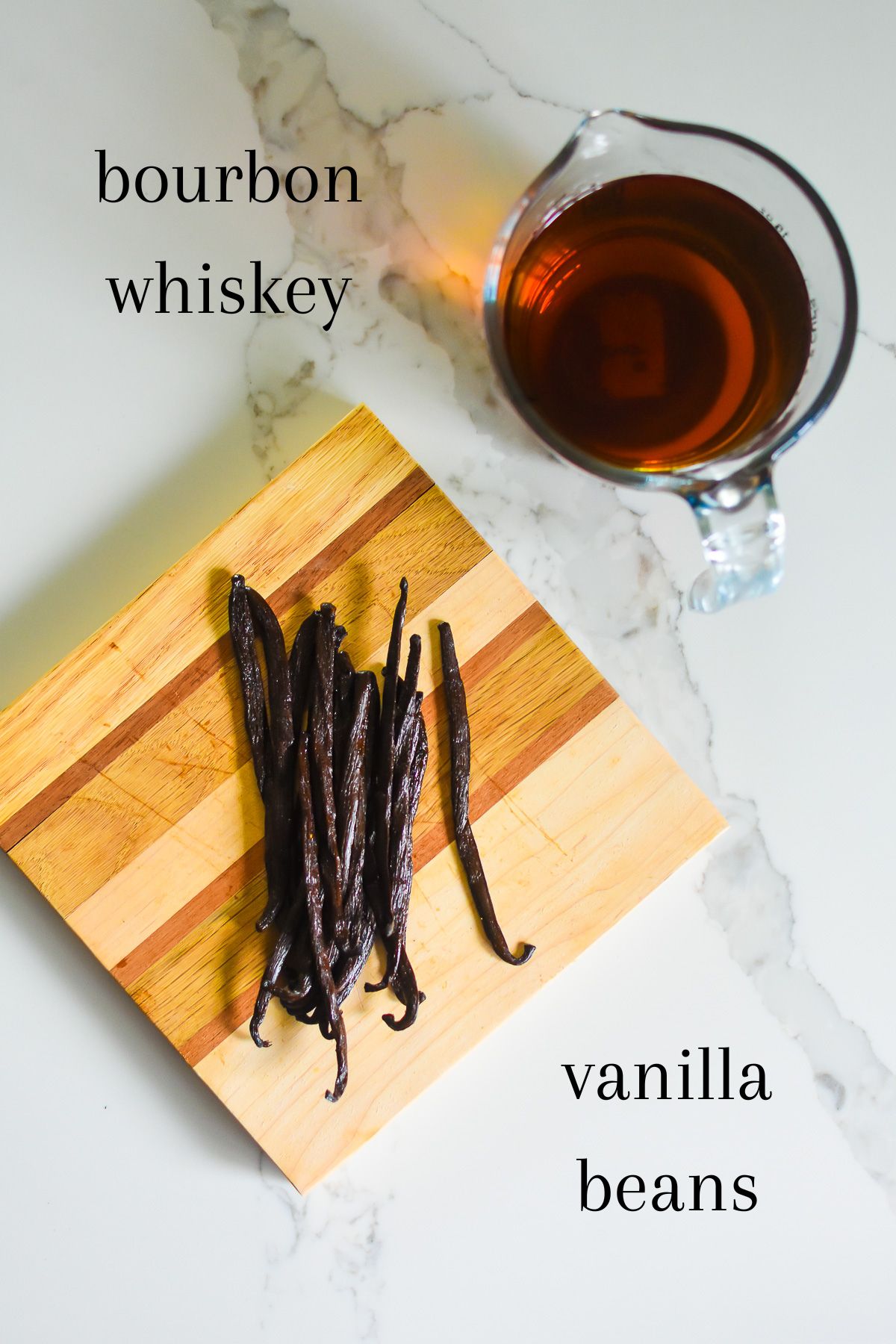 ingredients for a bourbon vanilla bean extract recipe on granite counter top: Kentucky bourbon whiskey and organic whole Madagascar bourbon vanilla beans on a wooden cutting board.