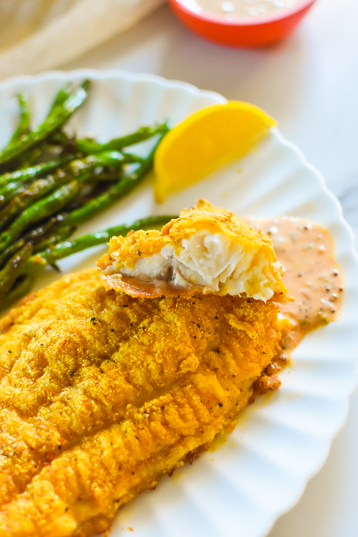 flaky crispy oven catfish served with to green beans and remoulade sauce on a white scalloped plate.
