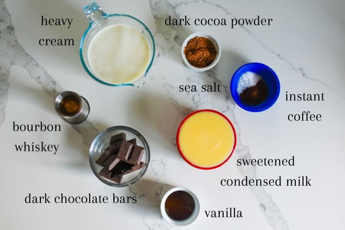 ingredients for making dark chocolate ice cream one granite counter top: heavy cream, dark cocoa powder, sea salt, instant coffee, sweetened condensed milk, vanilla extract, dark chocolate bars, and bourbon whiskey.