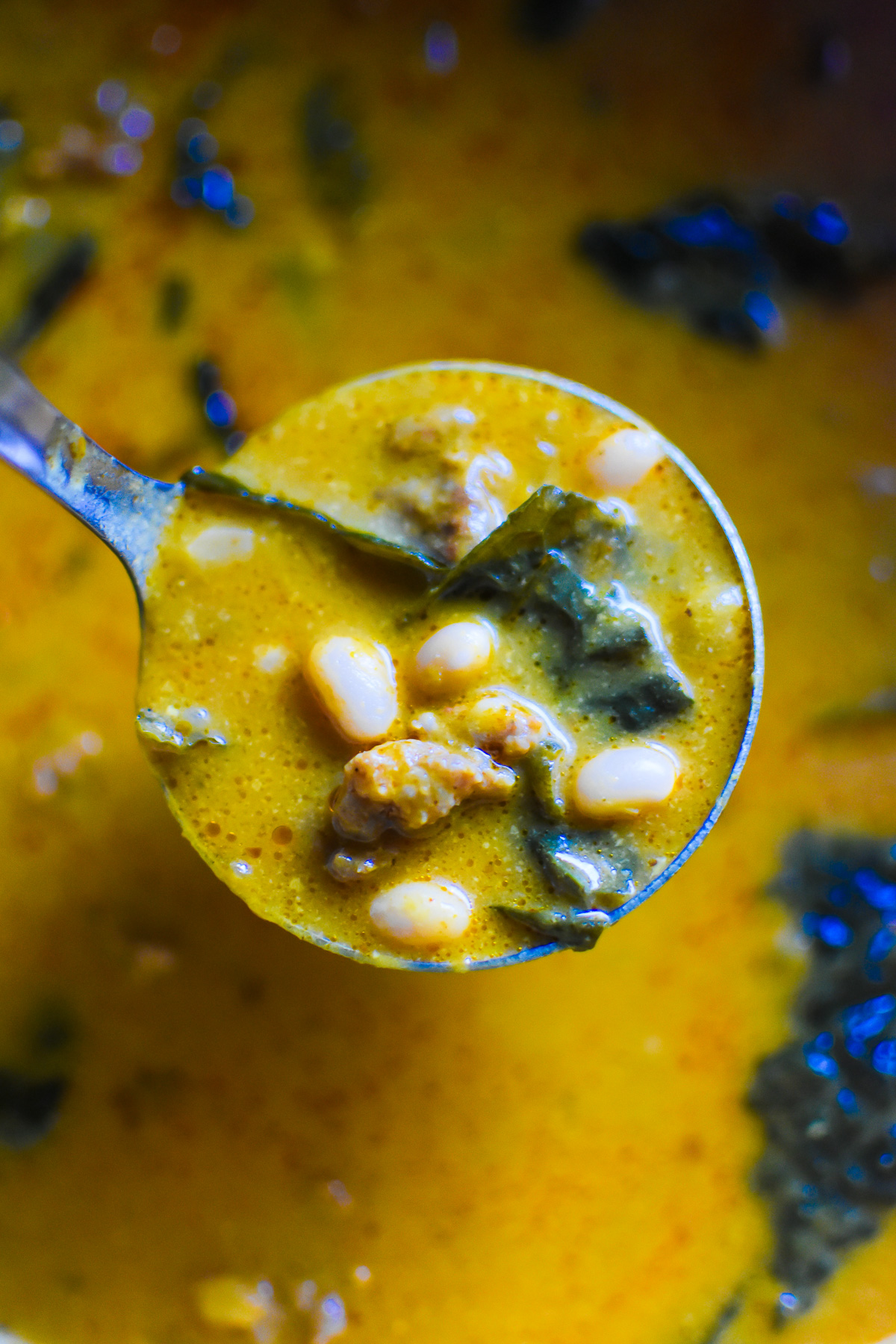 ladle of pumpkin soup from puree with kale, white beans, and spicy sausage crumbles.