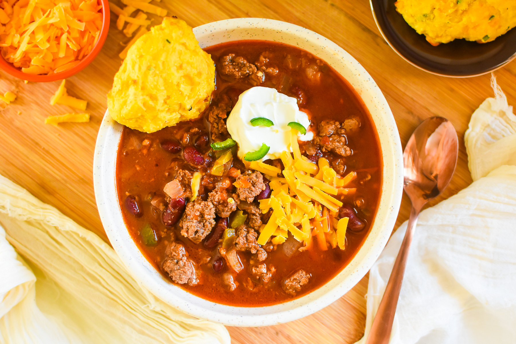 chili made with red kidney beans from scratch served in a stone bowl with sour cream, jalapeno, and cheddar cheese garnishes.
