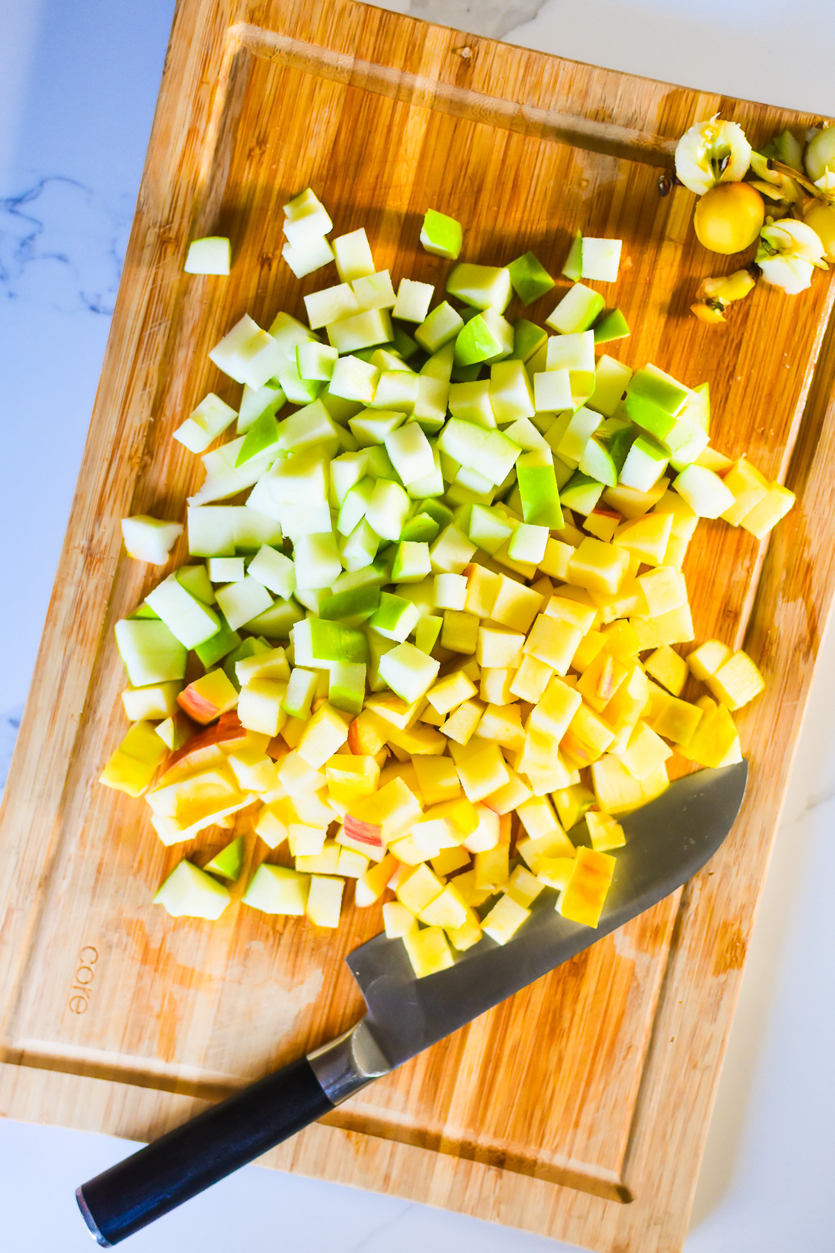 diced green and yellow apples on cutting board with chef knife.
