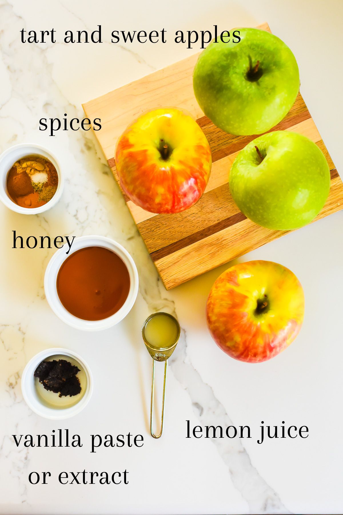 ingredients for making old fashioned spiced cooked apples on granite counter top: green Granny Smith apples, pink and yellow Honeycrisp apples, spices, honey, lemon juice, and vanilla bean paste.