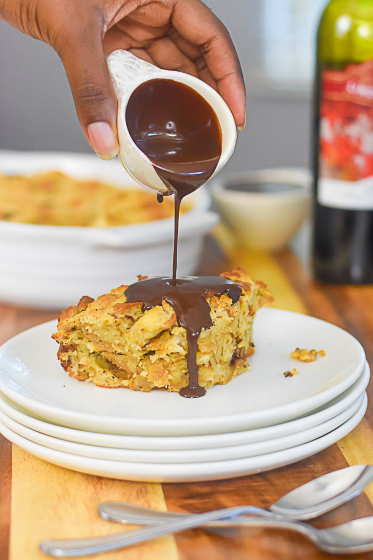 brown hand pouring dark chocolate red wine sauce on top of chunk of bread pudding.