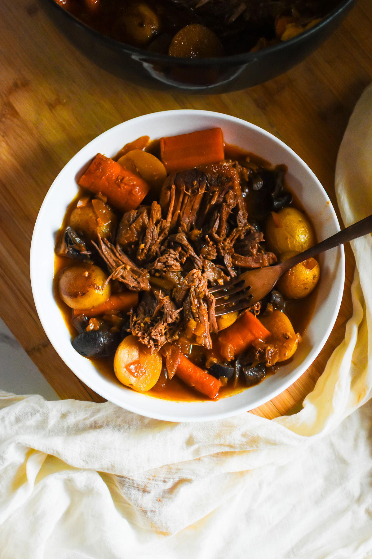 plate of melt-in-your-mouth pot roast served with au jus, golden potatoes, carrots, and mushrooms.