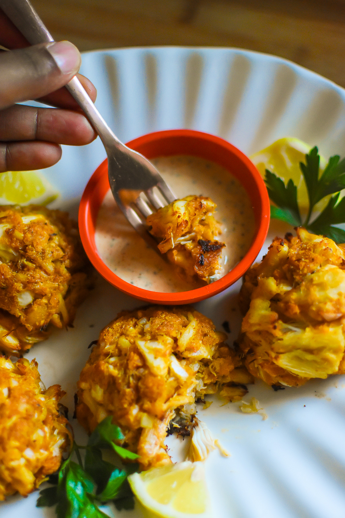 dipping piece of crispy oven crab cake in ramekin of Louisiana remoulade sauce.