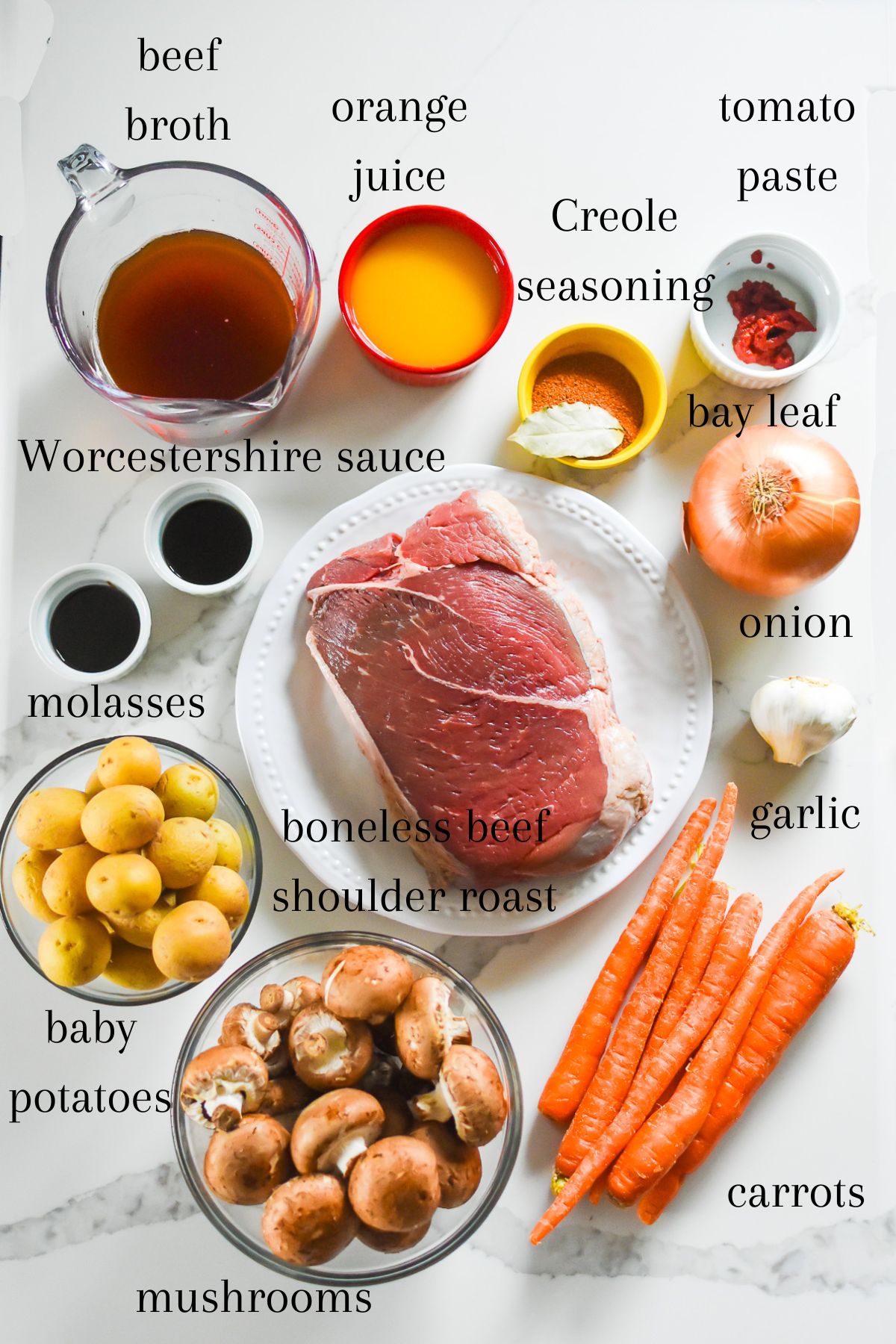ingredients for making Black pot roast at home: beef broth, orange juice, Creole seasoning, bay leaf, tomato paste, yellow onion, garlic, carrots, baby bella mushrooms, baby potatoes, boneless beef shoulder roast, molasses, and Worcestershire sauce.