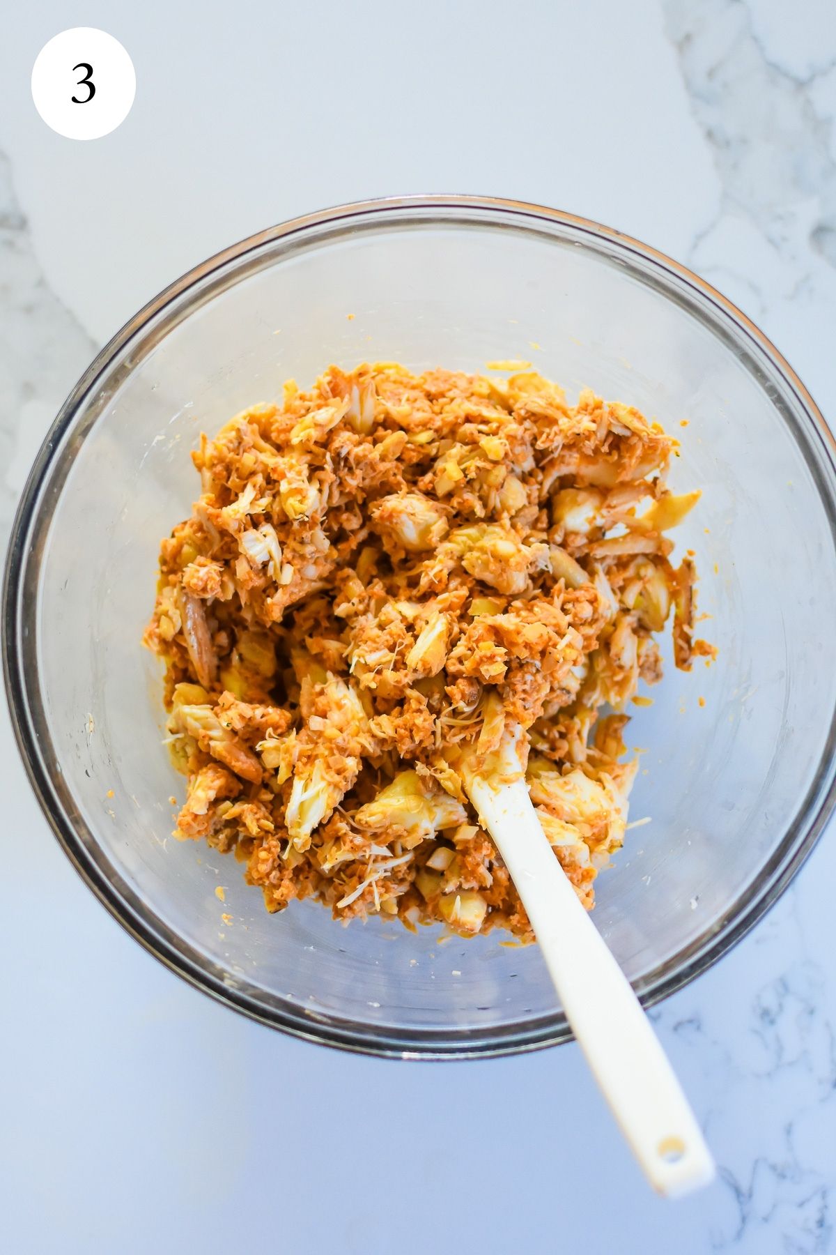 mixture of baked jumbo lump crab cakes in glass bowl with white silicone spatula.