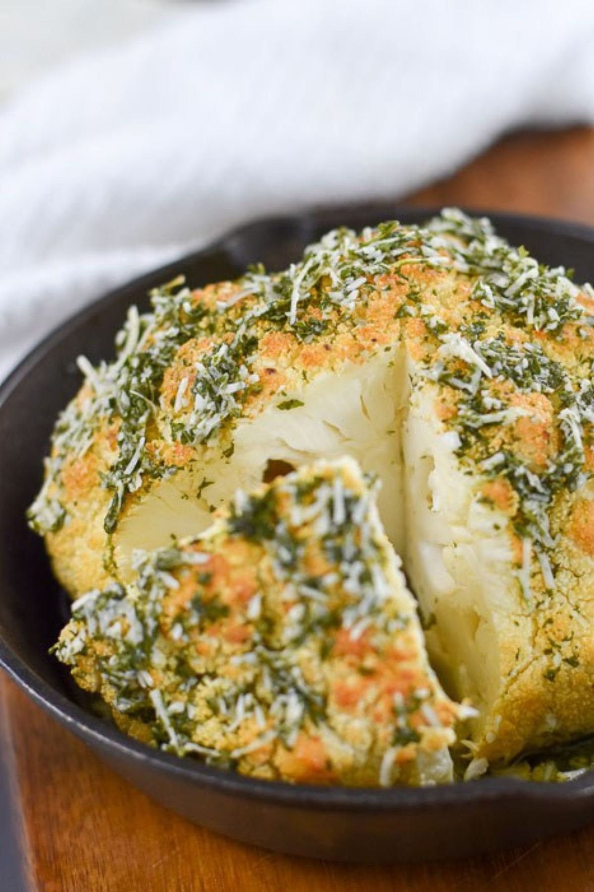 whole roasted cauliflower topped with herbs and parmesan cheese and cut into wedges.