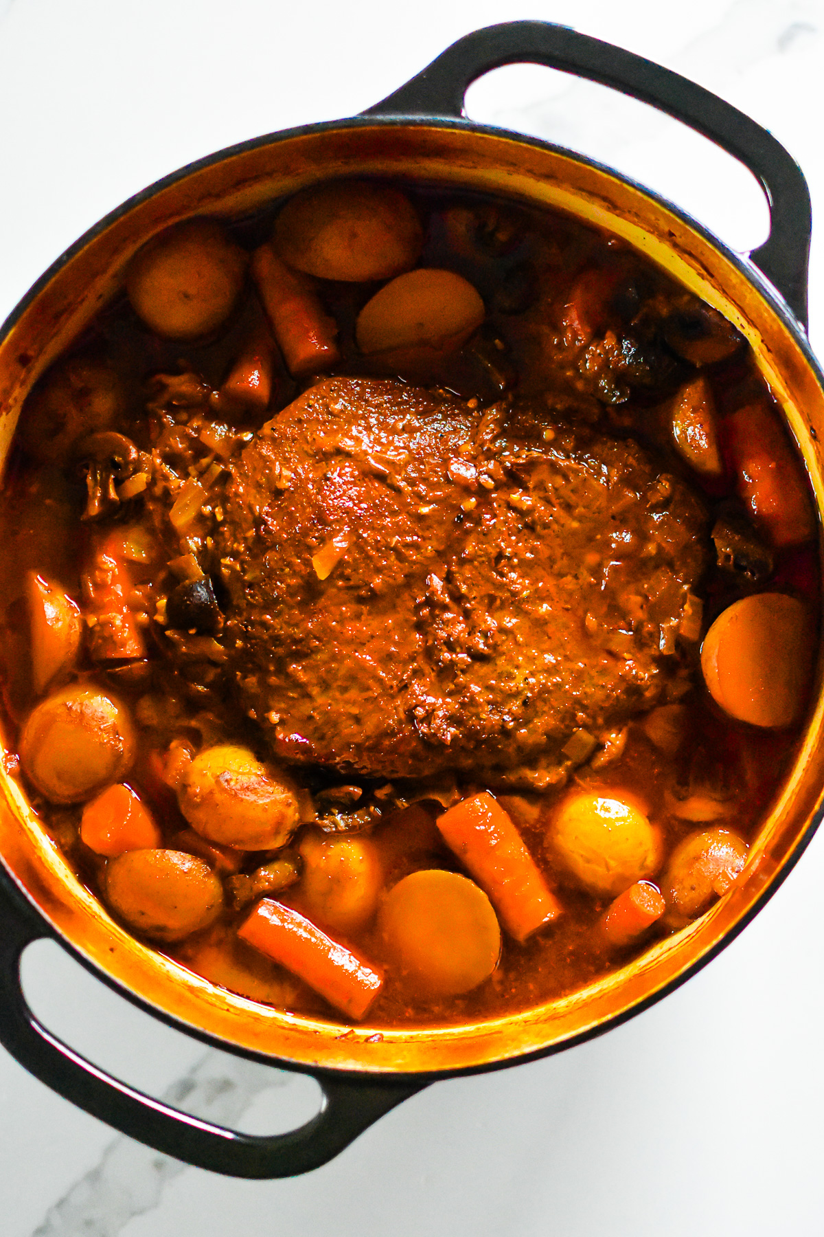 juicy braised pot roast in Dutch oven with pan sauce and chopped vegetables.