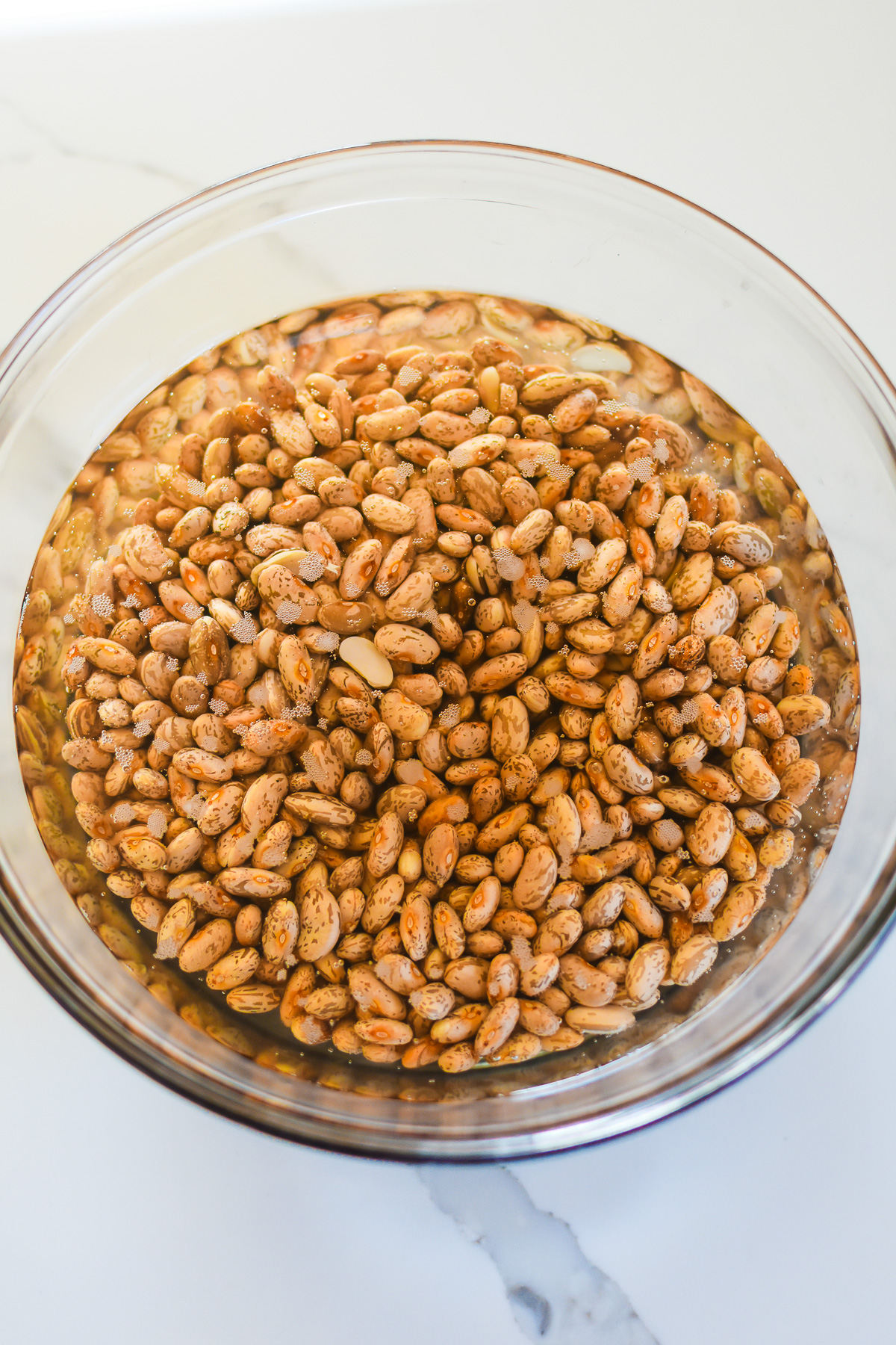 dried pinto beans soaking in bowl of water.