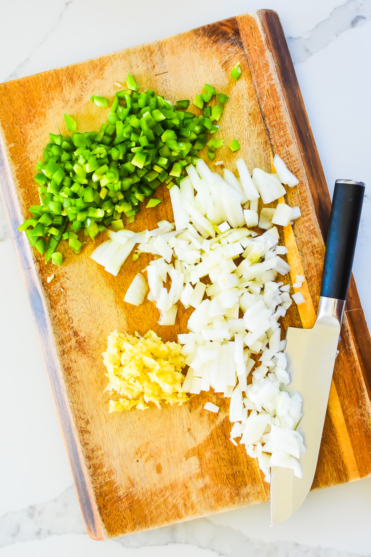 chopped onion, green chiles, and garlic on wooden cutting board with chef knife.