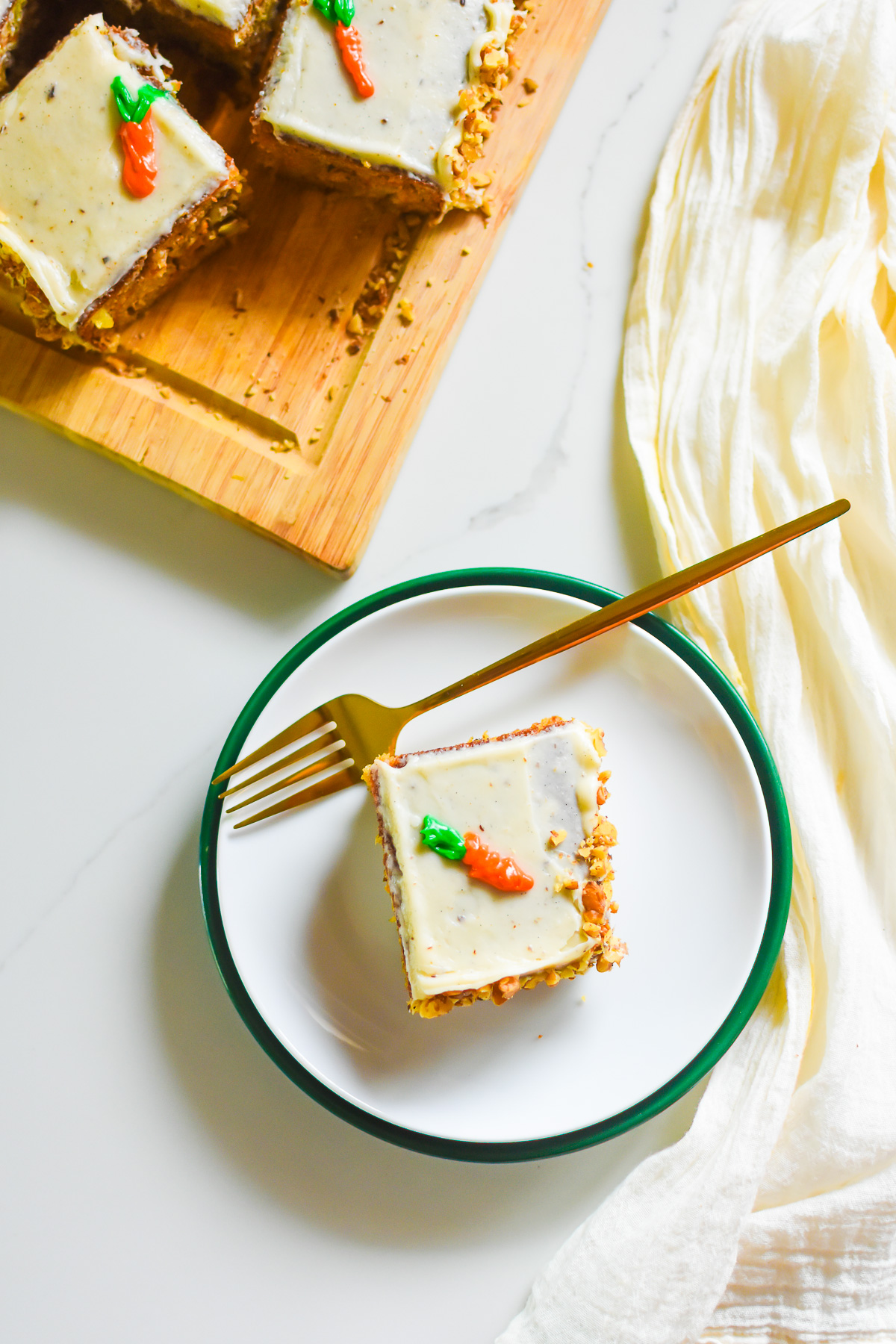 corner piece of carrot cake with cream cheese icing on a stack of saucers with a gold fork.