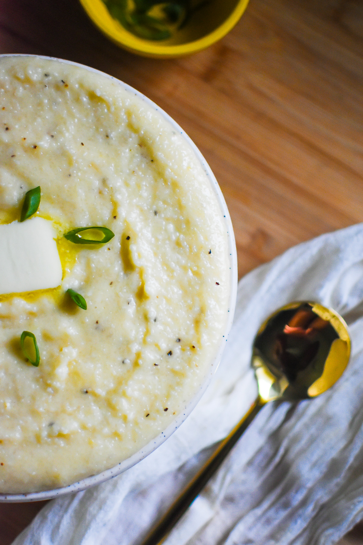 bowl of fluffy cheesy grits next to a gold serving spoon.