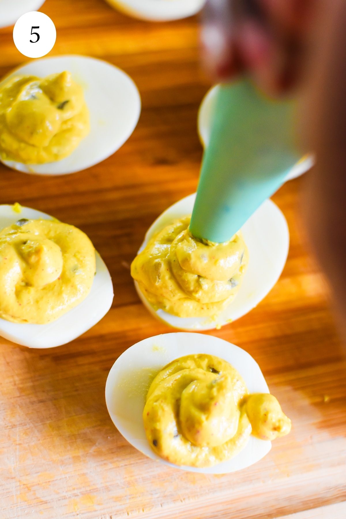 brown hand piping southern deviled egg filling to boiled egg whites.