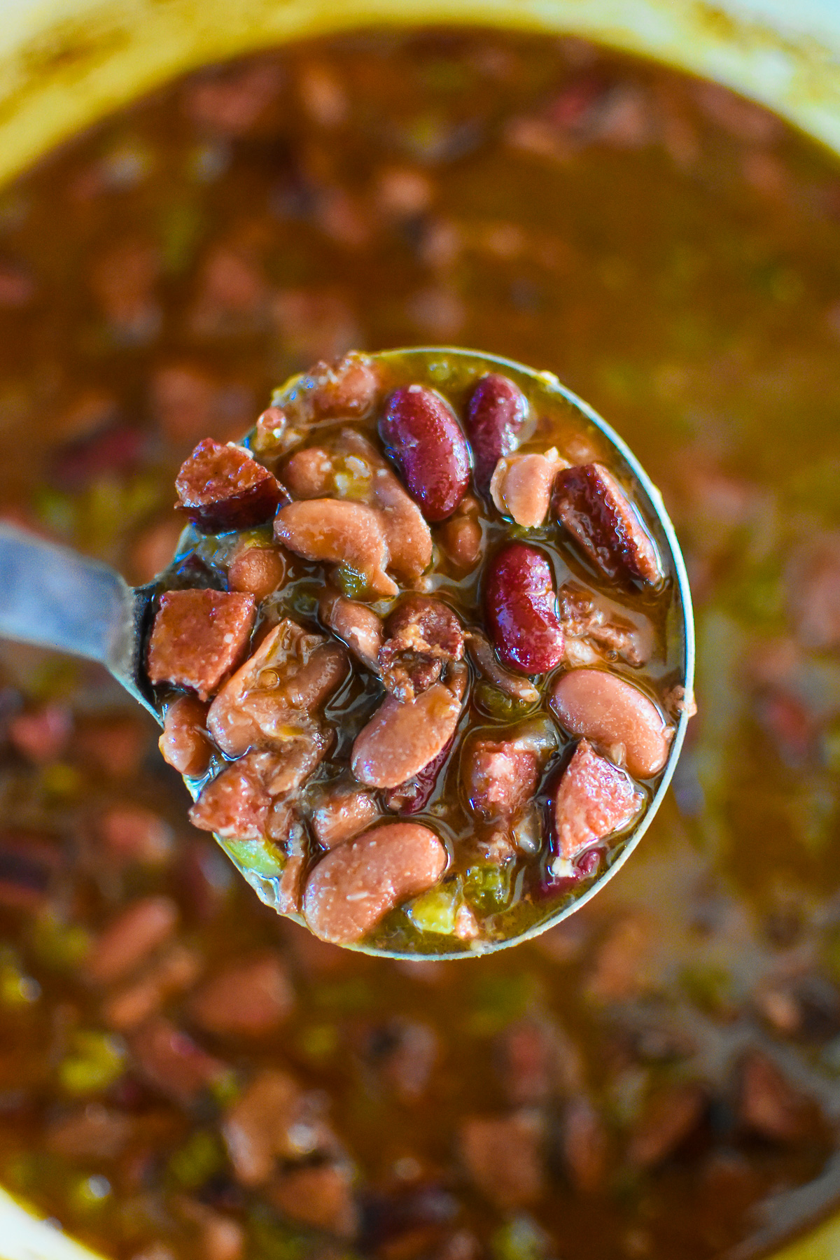 ladle full of Cajun style red beans with smoked bacon and Andouille sausage in sauce.